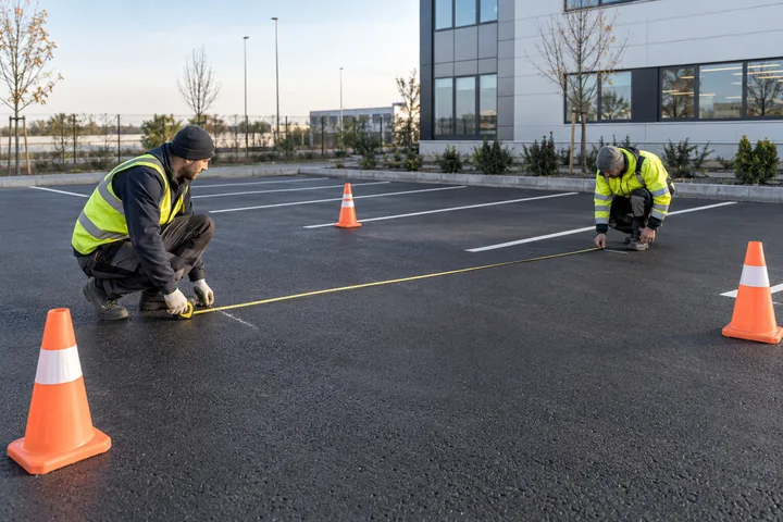 Trafiğe kapatılmış asfalt otoparkta çizgi yerleşimini şerit metreyle kontrol eden uygulama ekibi